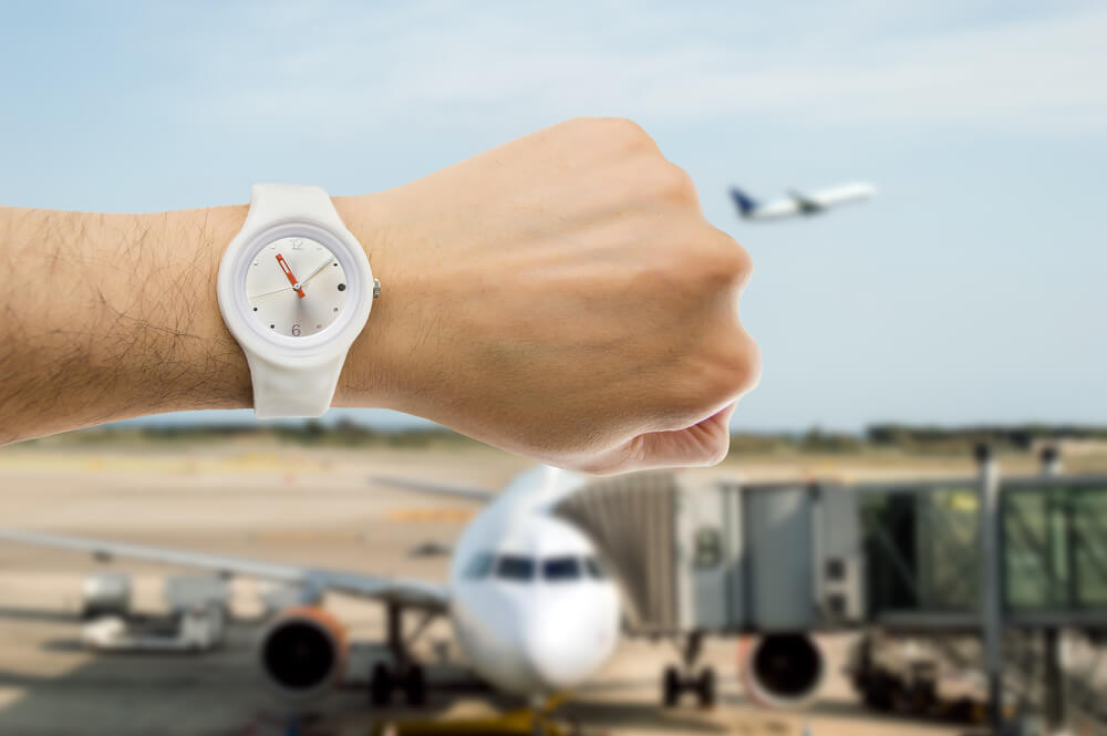 hand with wristwatch with airport in the background as the concept of punctuality in the transport