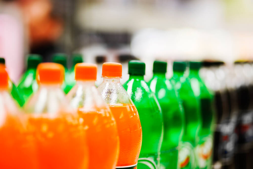 A long line of unbranded soda bottles in various flavors and colors, the focus on the center of the line.