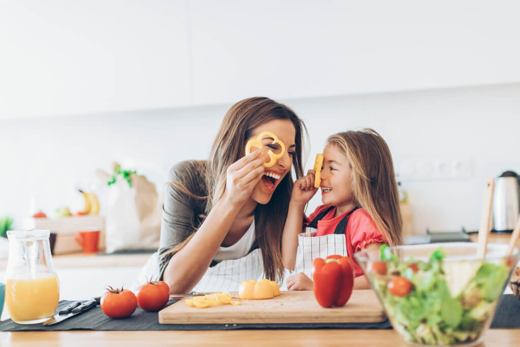 Mother and daughter having fun with the vegetables in the kitchen.
