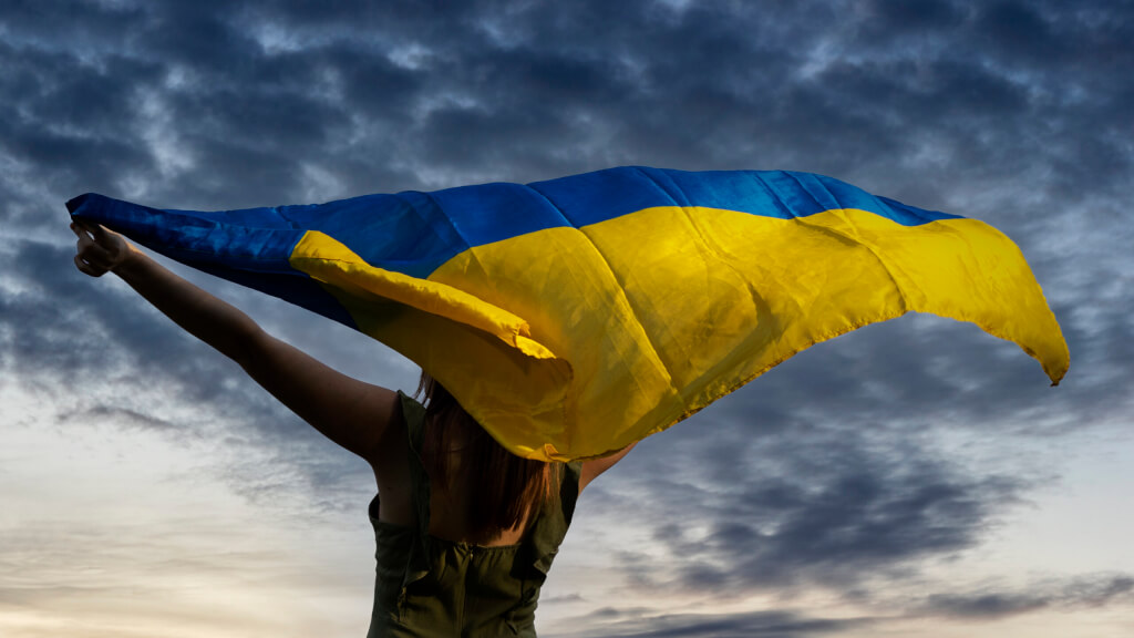 Woman holding yellow and blue flag Ukraine на pozadí dark cloudy sky.