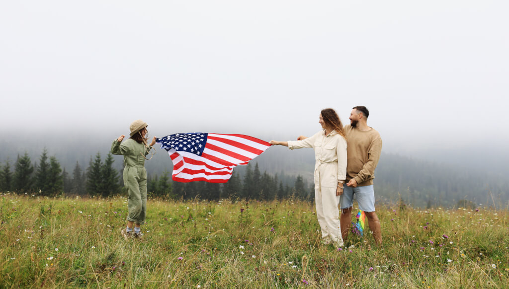 Happy family, parents and daughter child girl with American flag in nature on foggy mountains.
