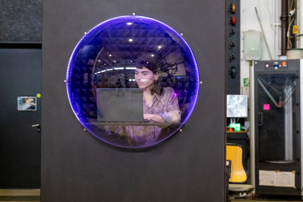 Businesswoman inside a small cubicle with a circular window using laptop at makers space