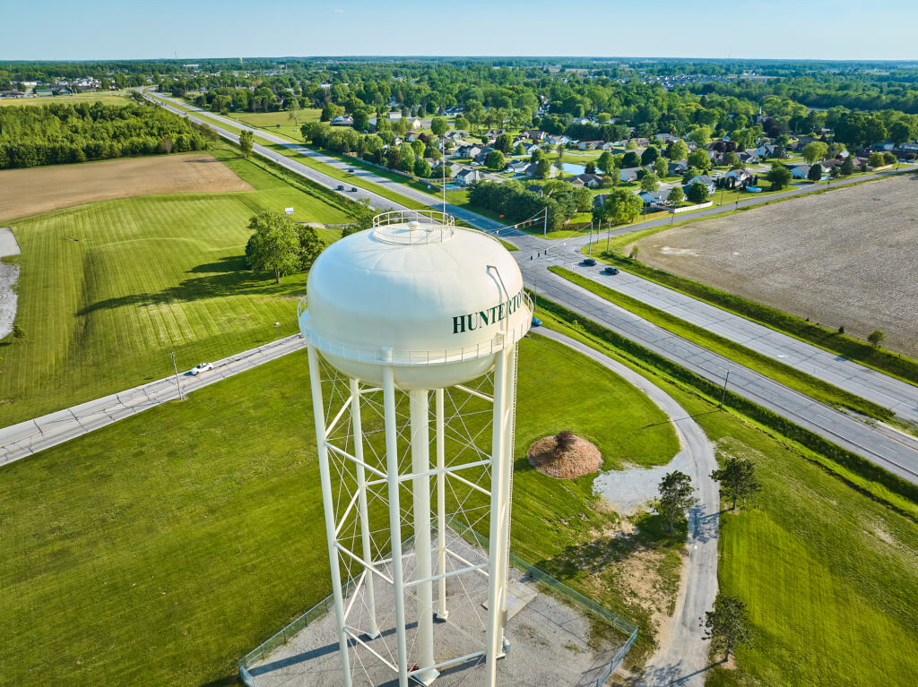 Aerial green fields around white water tower with nearby civilization