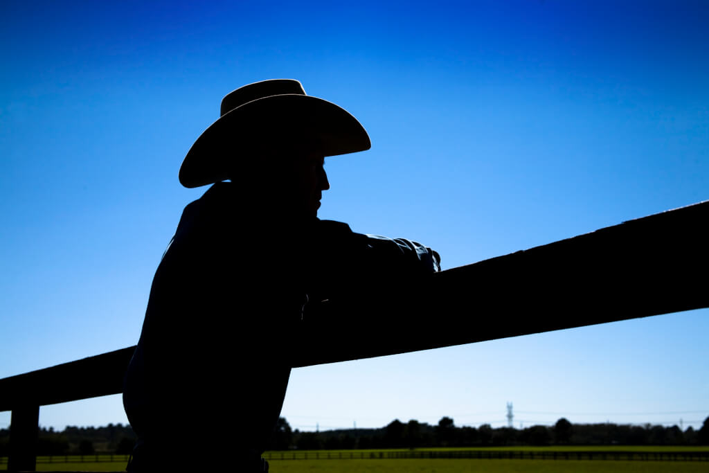 Silhouette of a rancher or farmer leaning on the ranch or farm fence. Cowboy hat. Man.