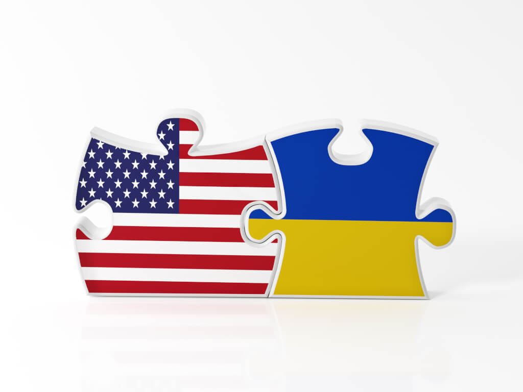 Jigsaw puzzle pieces textured with American and Ukrainian flags on white. Horizontal composition with copy space