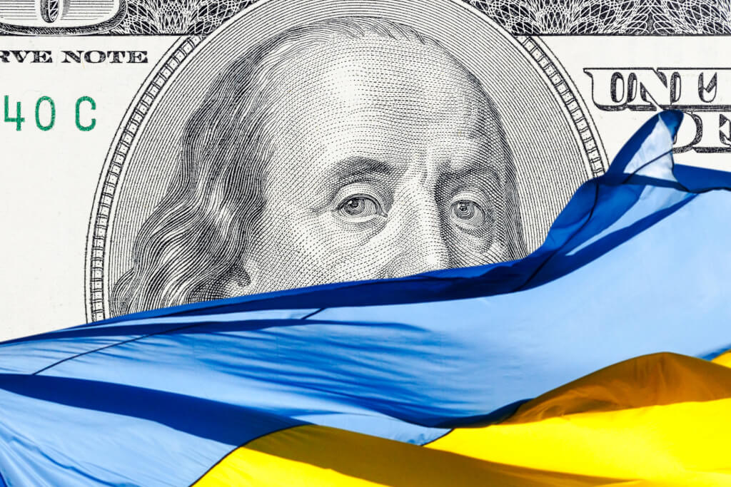 ukrainian national flag on foreground and US one hundred dollars paper currency on background