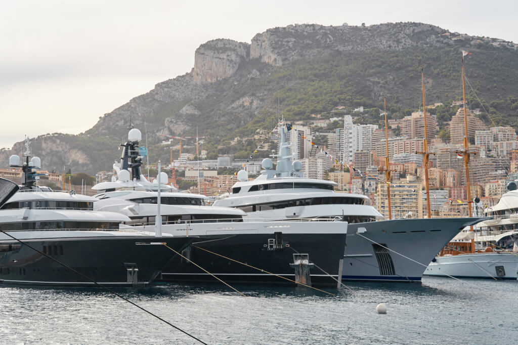 Few huge luxury yachts at the famous motorboat exhibition in the principality of Monaco, Monte Carlo, the most expensive boats for the richest people, mountain and residential complex on background