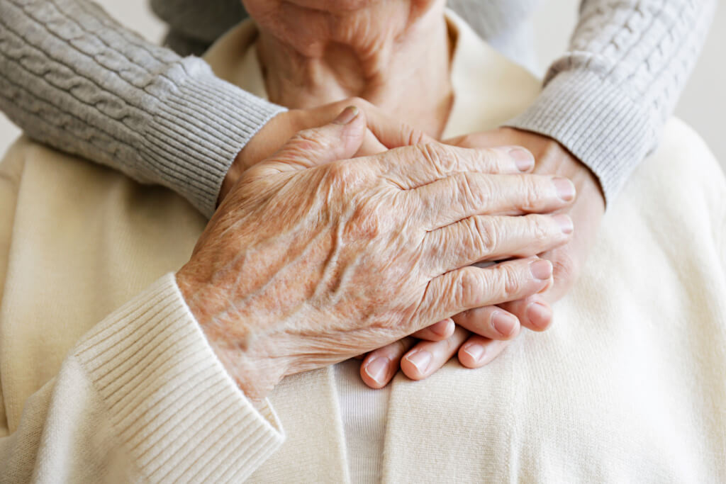 Mature female in elderly care facility gets help from hospital personnel nurse. Senior woman, aged wrinkled skin & hands of her care giver. Grand mother everyday life.