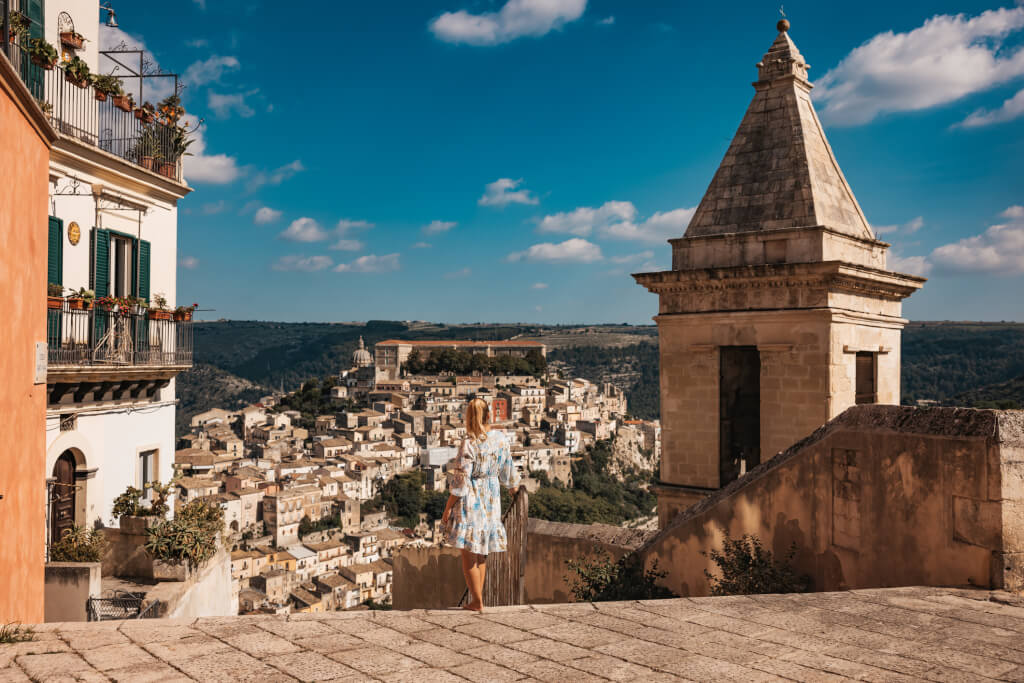 Rear view of female tourist walking on footpath by bell tower with cityscape in background on sunny day
