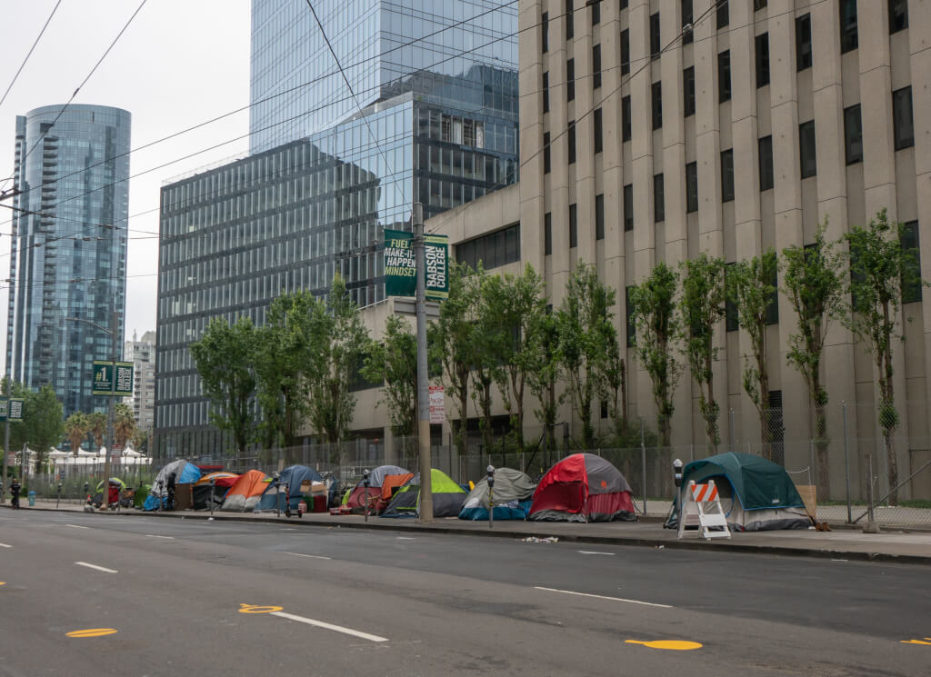 Homeless tents line Main Street in San Francisco's financial district during shelter in place order. Tents are surrounded by modern skyscrapers in an affluent area of the city.